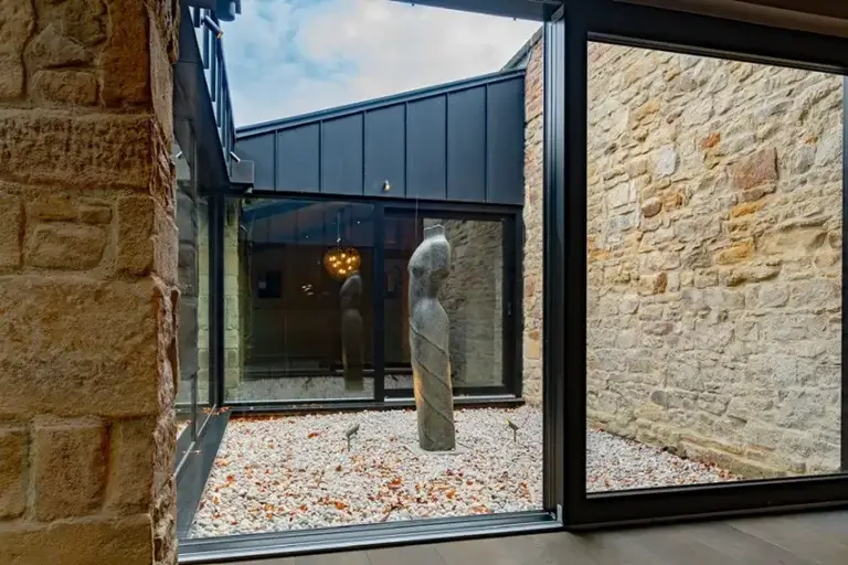 View through floor-to-ceiling glazing into an internal courtyard framed by restored stone walls and contemporary architecture.